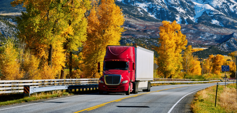 Truck driving down a road surrounded by autumn leaves